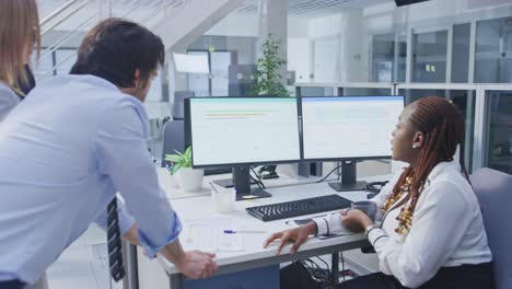 in the bright busy office group of young professionals have team building meeting. standing at the desk, discuss problem solutions, planning and strategizing, use digital tablets and desktop computers