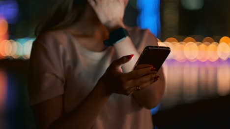 At-night-a-young-girl-sits-on-the-grass-in-a-big-city-and-looks-into-the-smartphone-screen-writes-a-message-and-maintains-her-personal-blog.