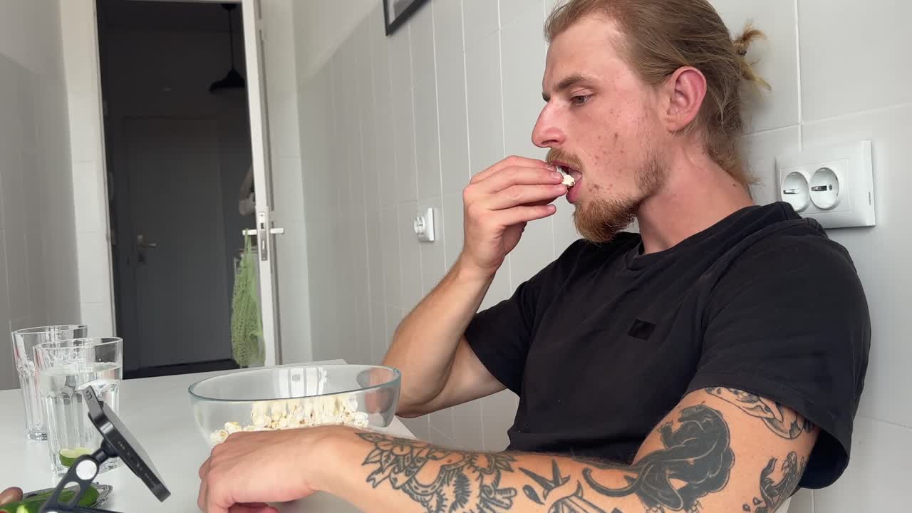 Jovem homem comendo pipoca e assistindo a conteúdo no celular