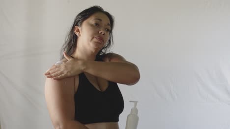 latin adult woman applies cream on reddened sunburned shoulder skin