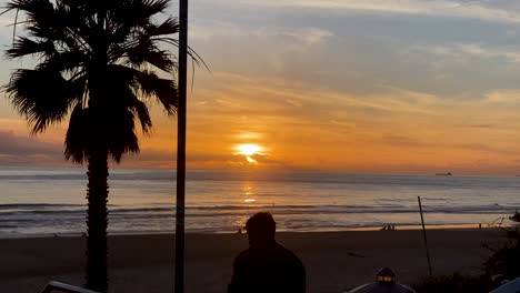 silhouette-of-man-at-Carcavelos-beach,-Slowly-waves-form-and-break,-beautiful-Atlantic-ocean,-deep-yellow-sunset-on-water-reflections,-Portugal