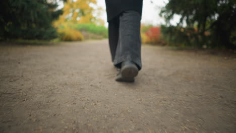 close-up de pernas caminhando em um jardim durante o outono, vestindo jeans pretos e sapatos de lona, capturando a essência de um passeio tranquilo entre folhas de outono