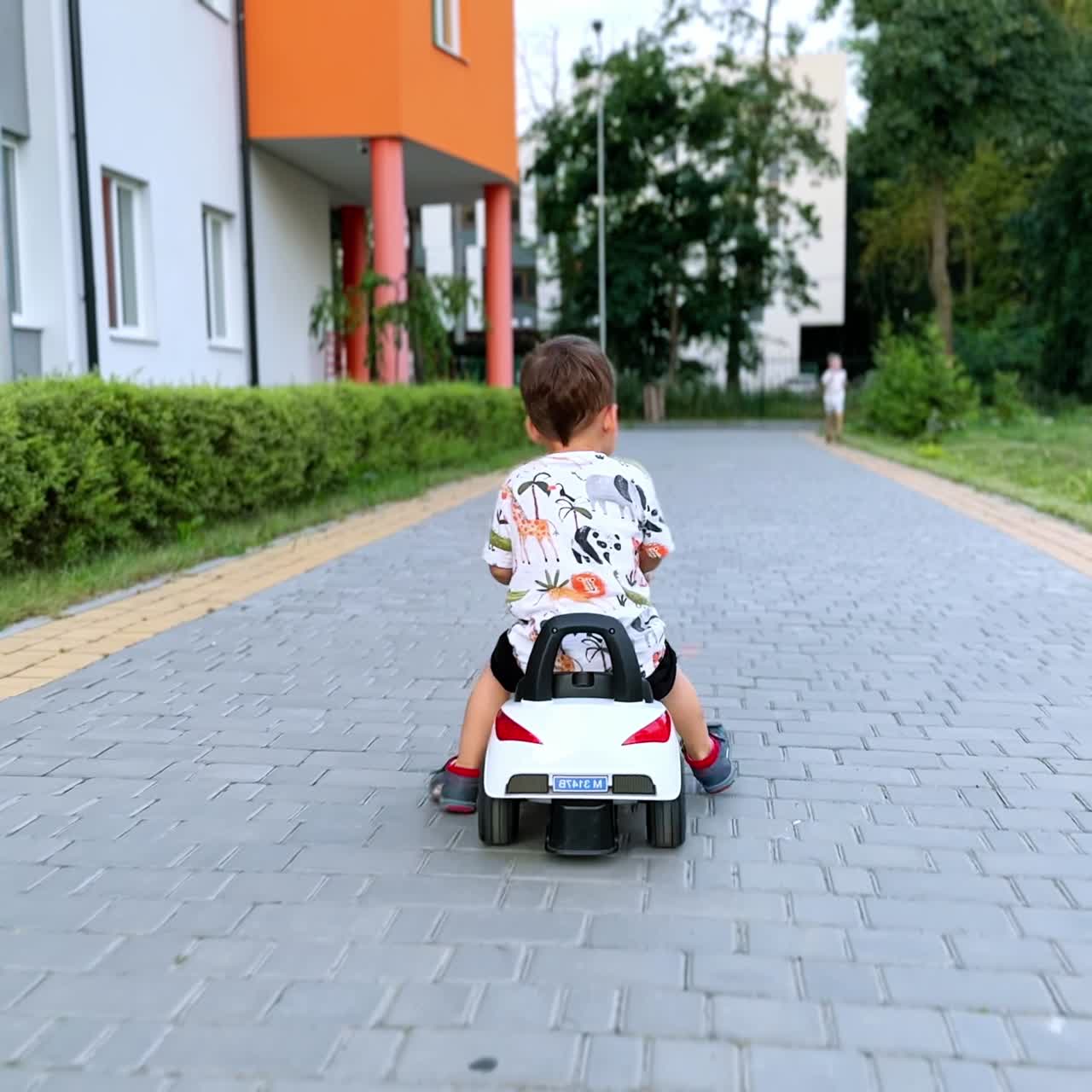 Vista posteriore di un neonato che guida un'auto giocattolo all'aperto. Il bambino muove velocemente i piedi per spingere da terra e guidare