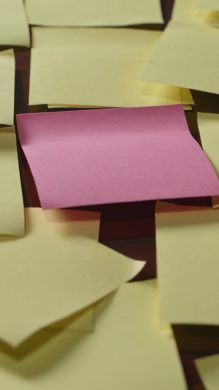Vertical video: Starting camera moving closer to pink note on desk revealing pale yellow notes
