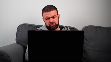 Middle-Eastern-Man-Sitting-On-Sofa-And-Staring-At-Laptop-At-Home