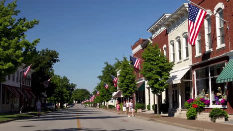 sunny main street with american flags, pedestrians, and a vintage car