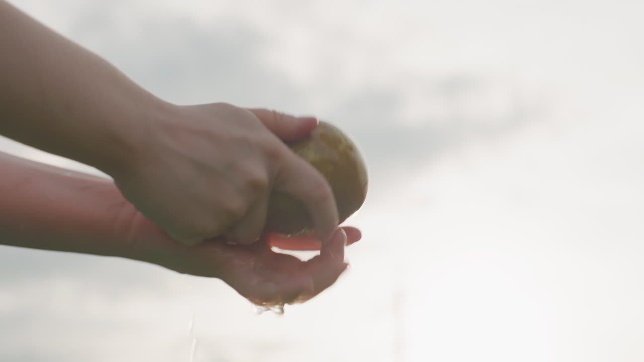 close up hands rinsing pear under stream of water outdoors soft light background, healthy fruit cleaning, summer scene, gentle care, healthy summer snack preparation