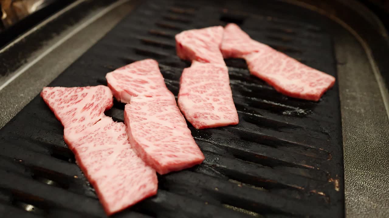Primo piano di fette di manzo wagyu marmorizzato di alta qualità che sfrigolano su una calda griglia barbecue nera.
