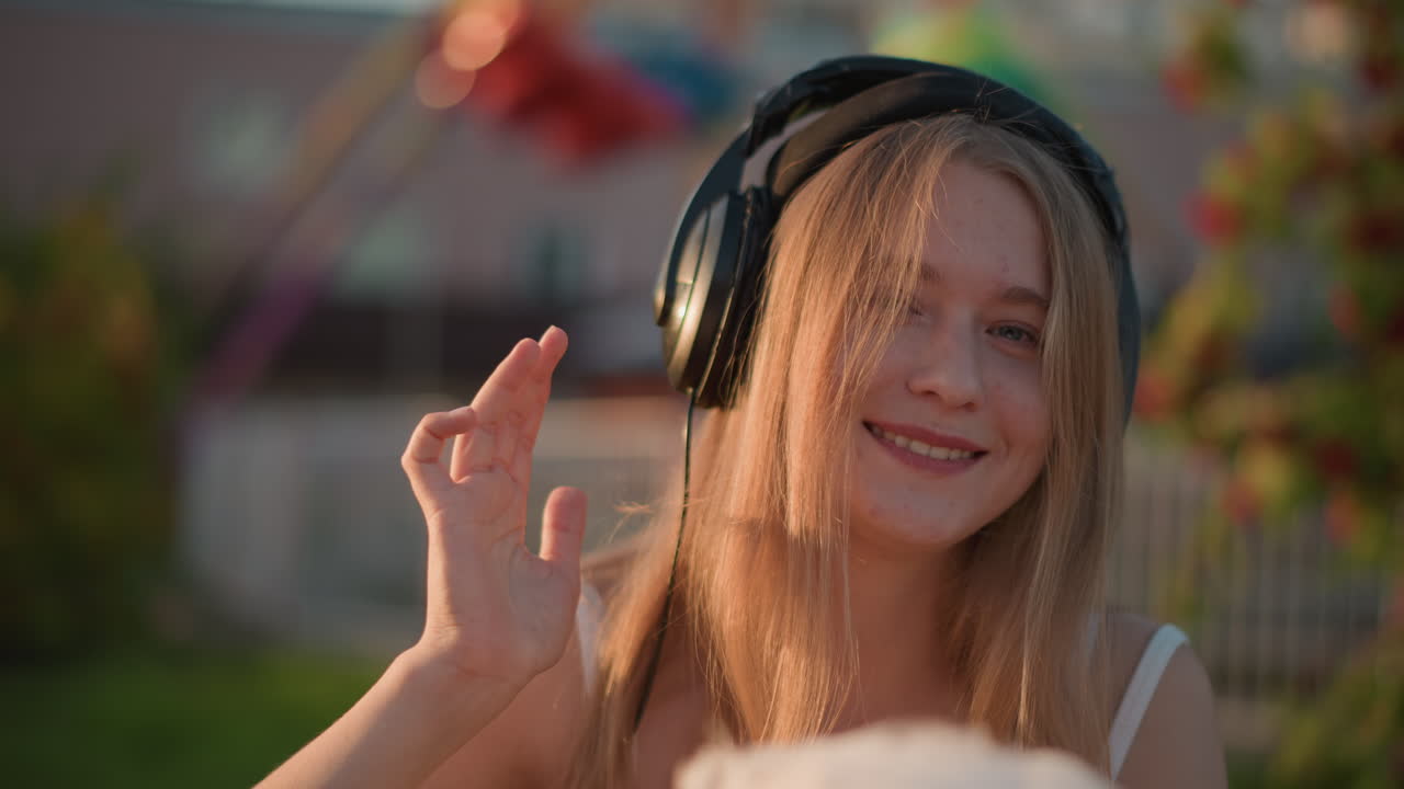 ragazza bianca in una fiera dorata, che balla immersa nella musica, mano all'orecchio, ondeggio ritmico, assaggia lo zucchero filato, aspirante DJ piena di energia, fantasia di ballerina di strada, risata spontanea, luci calde della sera, bokeh