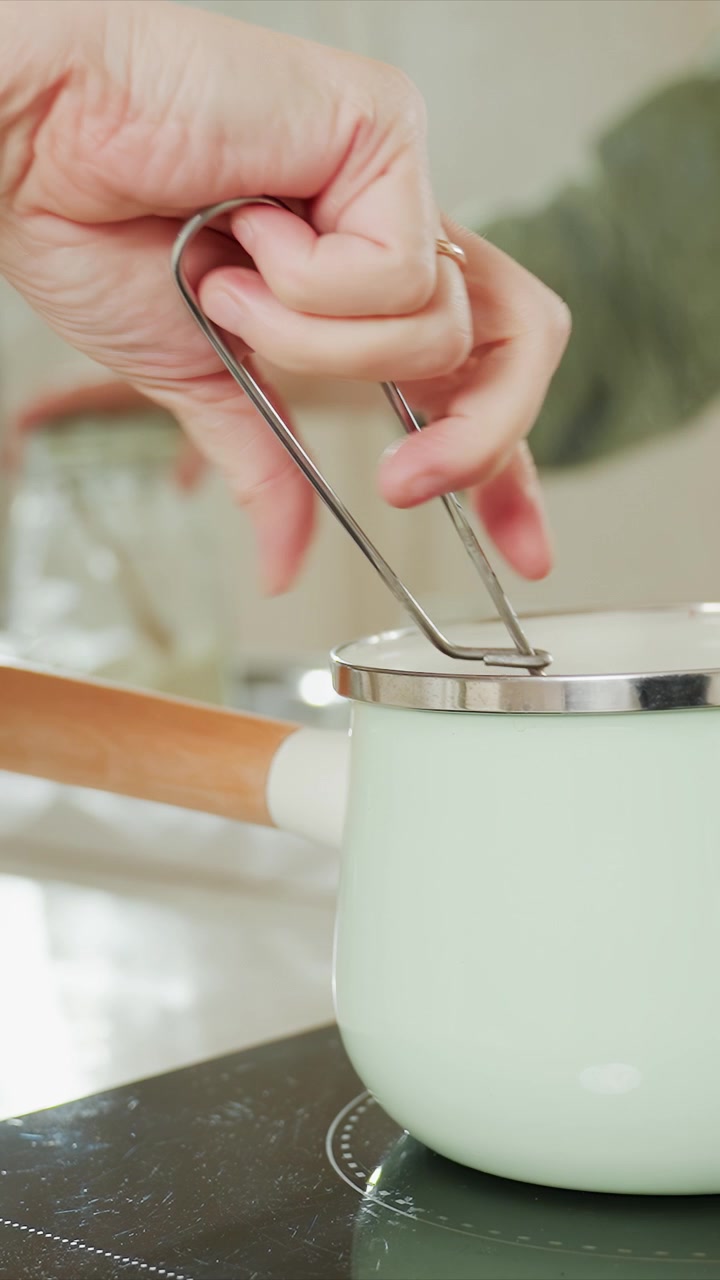 Close up of hands performing cooking actions. Hand stirs contents using tongs while another person handles jars. Scene remains focused in kitchen environment showing pot