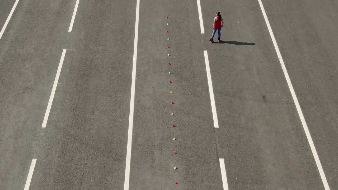 Woman athlete rides on roller skates, makes a figure eight by kicking. Slalom elements, criss cross. Aerial view, professional roller skating training. 4k, 10bit, ProRes