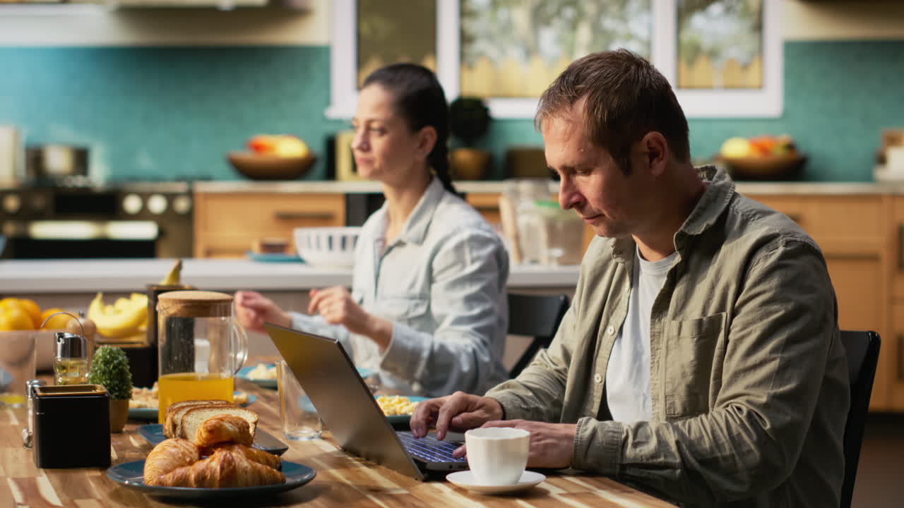 Busy working dad typing on laptop at kitchen table with his family