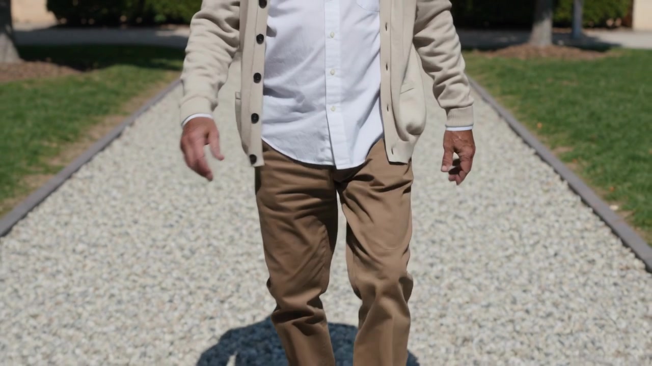 Lifting left leg, adult man walking toward camera on pebble path, showing brown shoes