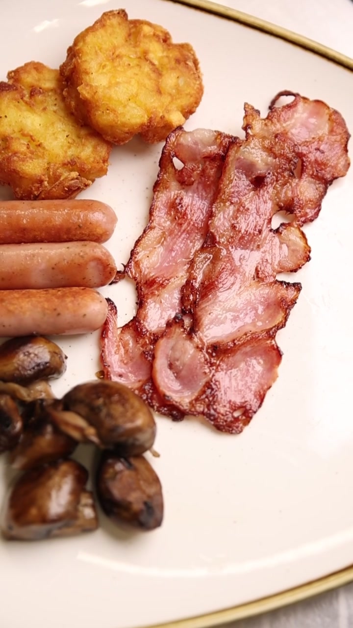 Delizioso piatto per la colazione con pancetta croccante, salsicce, hash brown e funghi