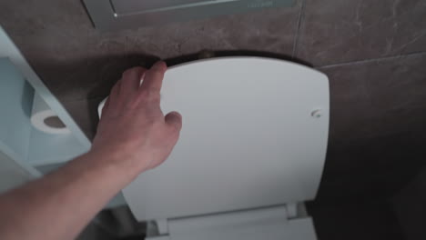 presionando a mano el botón de descarga del inodoro y cerrando la tapa, filmado en primera persona con una cámara portátil