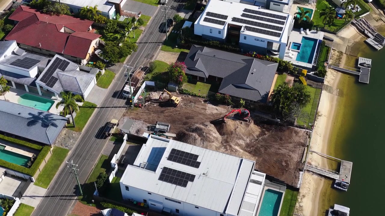 High angle drone shot of canal houses and an active excavator on a dirt lot.