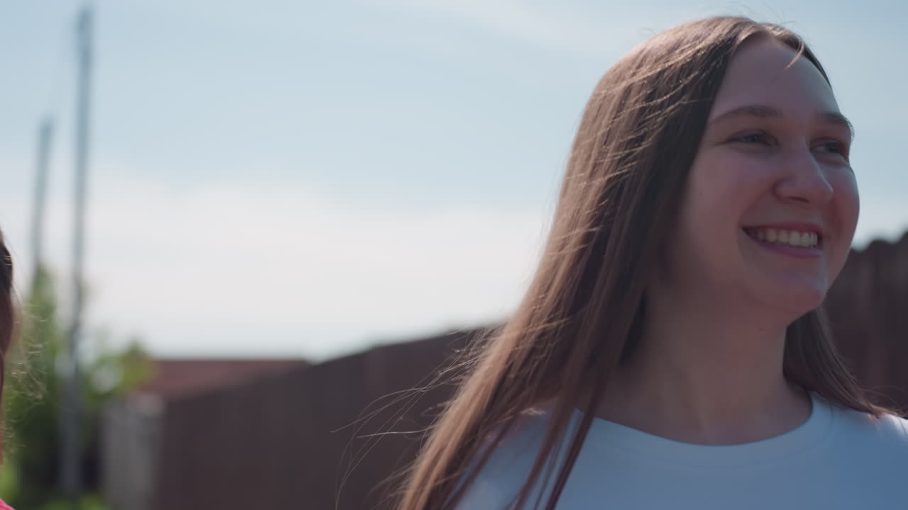 Young woman wearing black sunglasses and red shirt having cheerful conversation outdoors under sunny sky, captured in close up with soft natural light and blurred rustic background