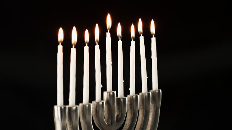 Silver menorah with nine white, lit candles burning in it, seen at an angle, close up, lockdown