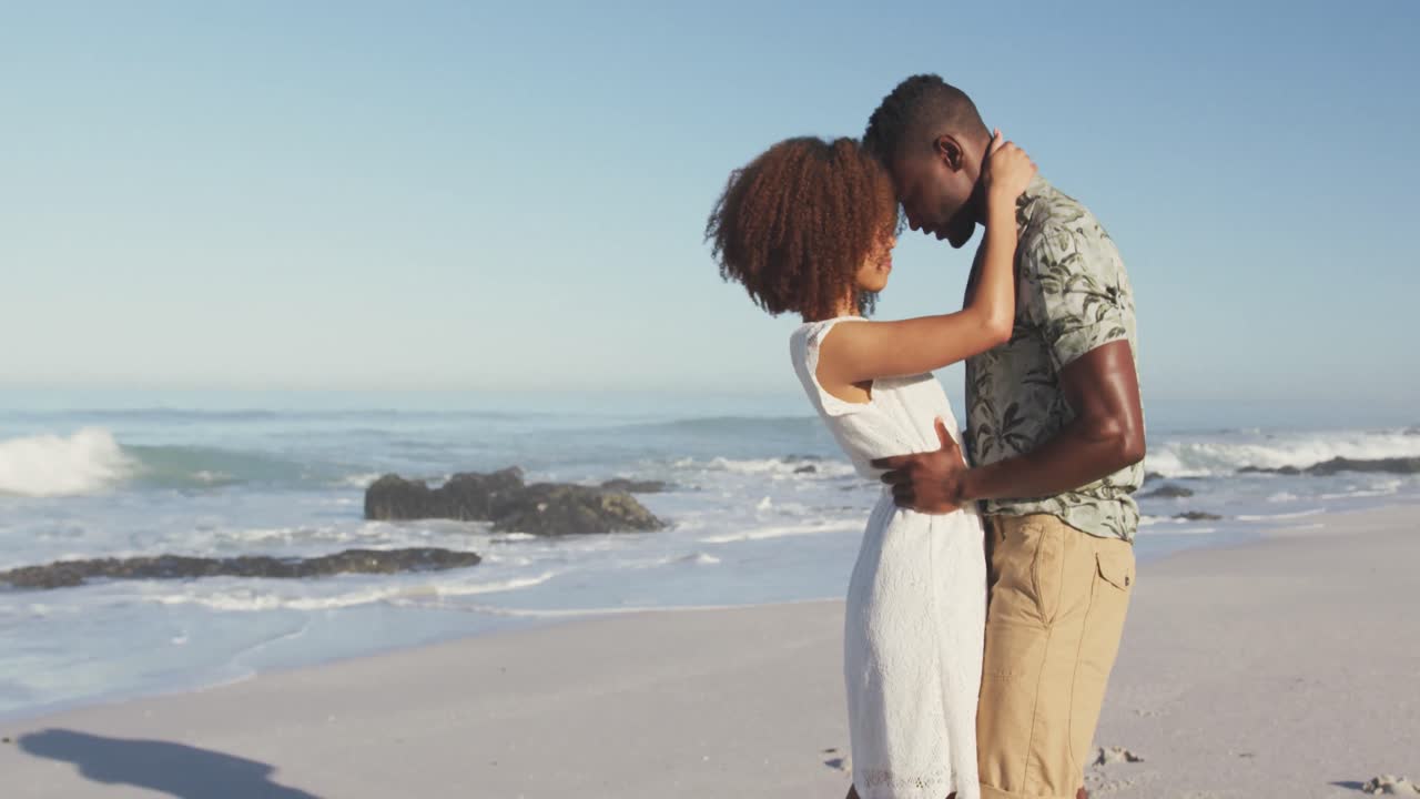 una pareja afroamericana acurrucada en la playa.