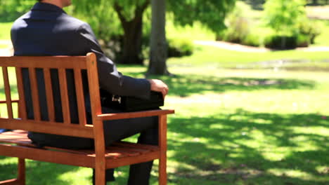 Businessman-sitting-down-on-park-bench-