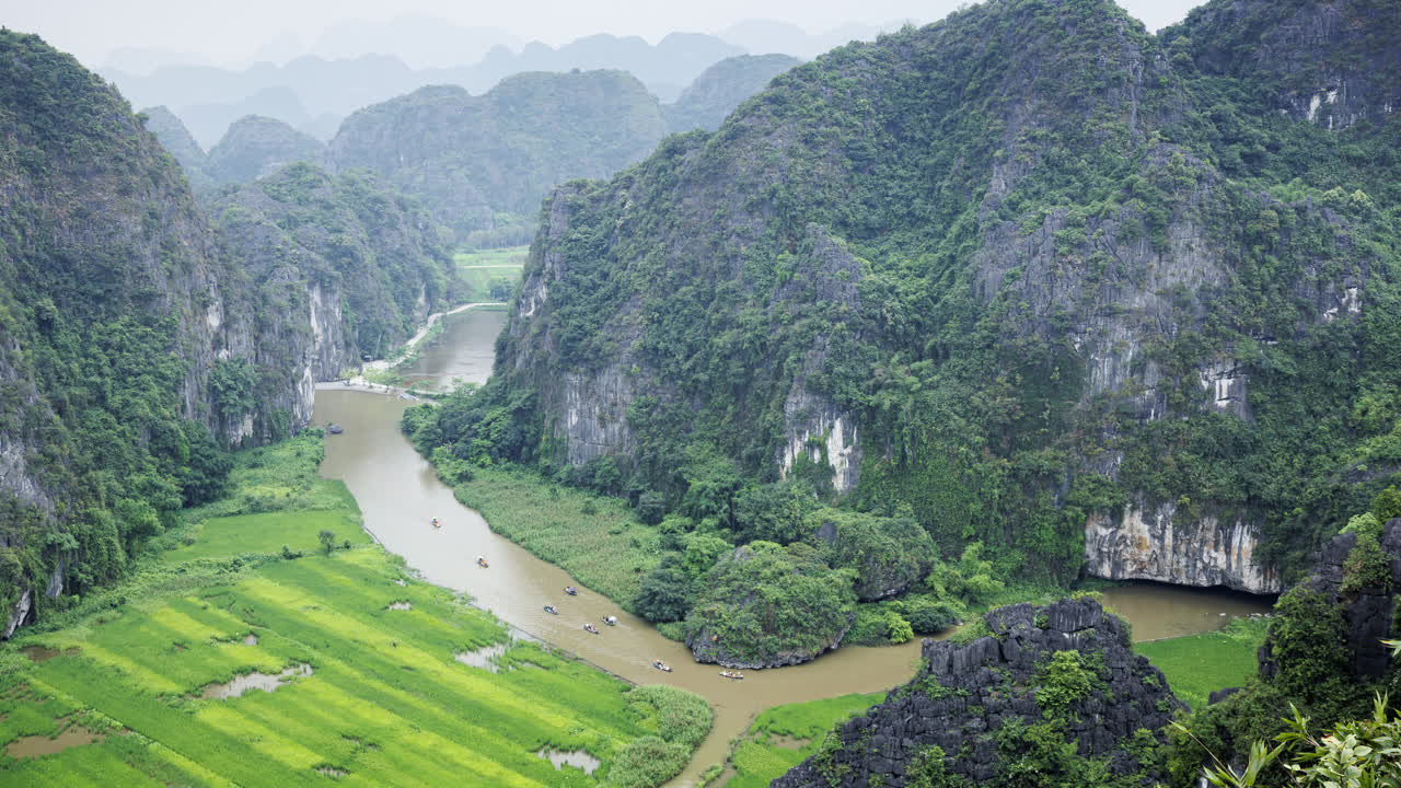 A zoom-out timelapse from Ninh Binh’s scenic river reveals traditional tourist boats and dramatic mountain landscapes surrounding the waterway