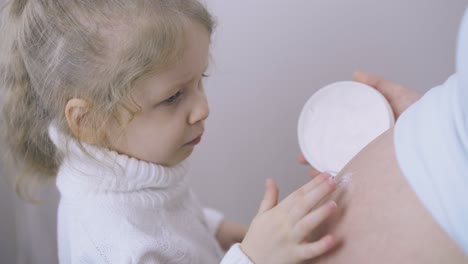 little girl applies cream on pregnant mother tummy by finger