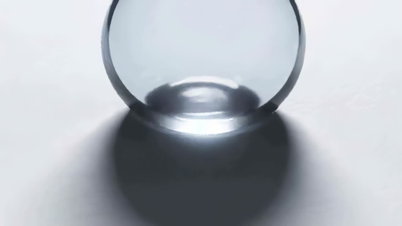 Gravity pulling transparent liquid drop downward, contacting white surface, forming rim and puddle
