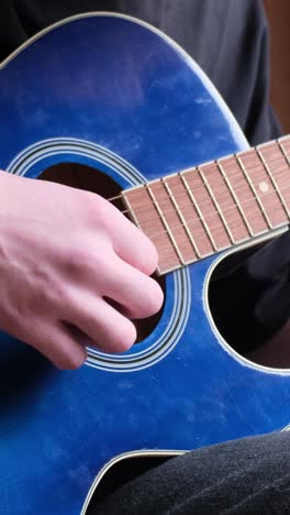 a male musician plays a blue acoustic guitar. modern young hipster guitarist playing guitar. stylish curly hair.