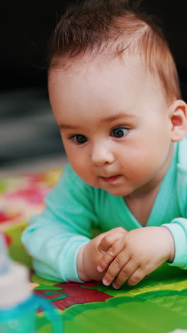focused baby boy with his hair up crawling to the bottle. funny little kid moving purposely by the colorful mat on the floor. vertical video