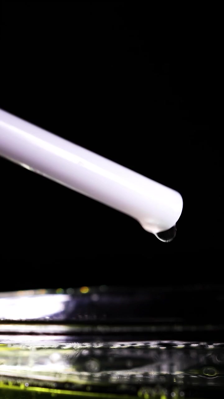 Una bacchetta bianca interagisce con un liquido, formando bolle di sapone in un ambiente scuro con superfici riflettenti.