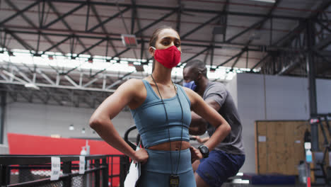 Entrenadora-De-Fitness-Femenina-De-Raza-Mixta-Con-Mascarilla-En-El-Gimnasio