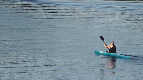 a female athlete paddles down a river in a canoe, showcasing strength and focus. the river is calm, and the surrounding nature adds to the serene atmosphere