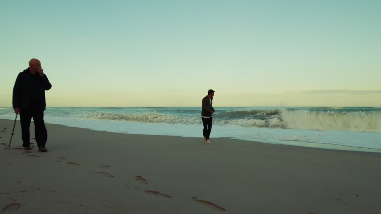 Two Men in Silhouette Walking on the Beach During a Stormy Sea Waves