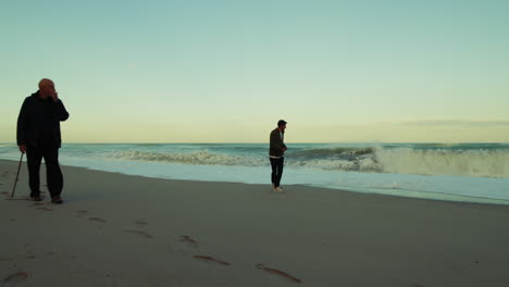 Two Men in Silhouette Walking on the Beach During a Stormy Sea Waves