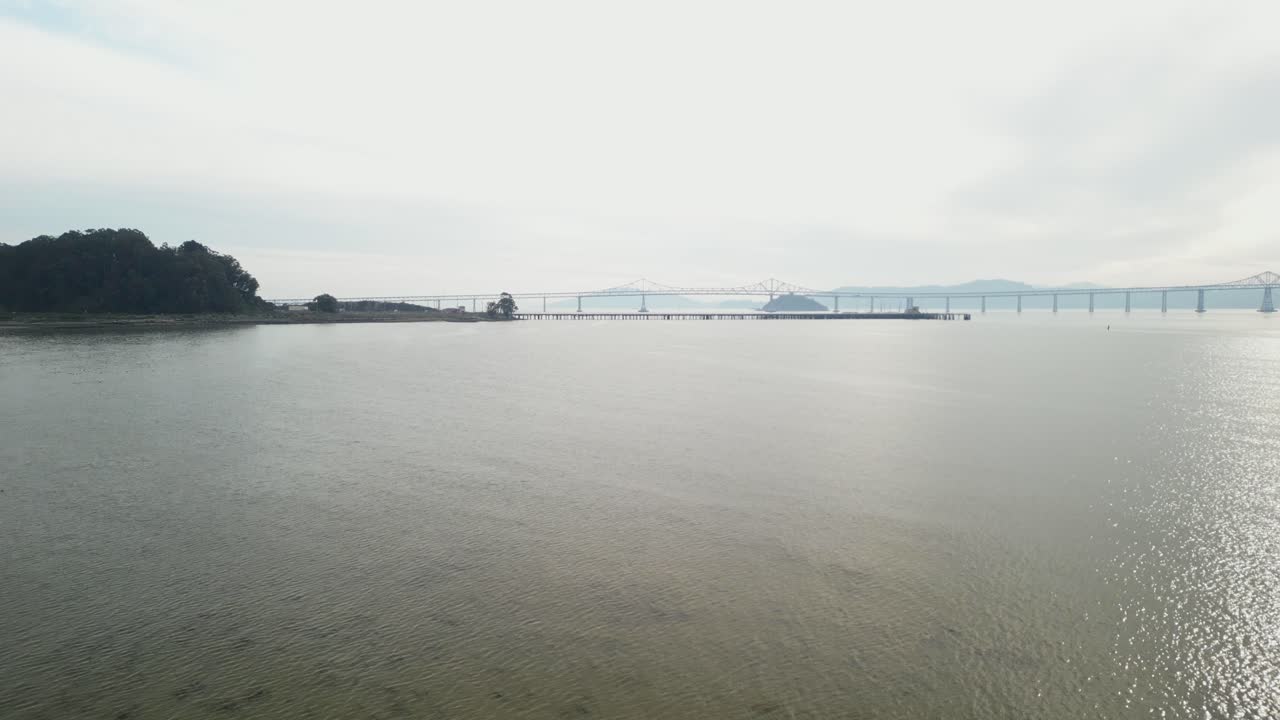 Drone ascends above glistening waters with Richmond Bridge in view from Point Molate Beach Richmond California USA