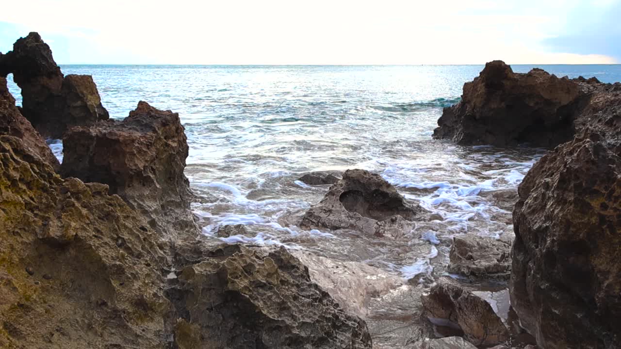 Potenti onde atlantiche si infrangono e si avvolgono tra affilate formazioni rocciose su una costa portoghese, creando acqua bianca spumeggiante e un dinamico movimento costiero sotto la luce del giorno.