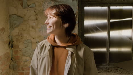 portrait of a redhead girl looking at camera while touching her hair and smiling in a ruined building