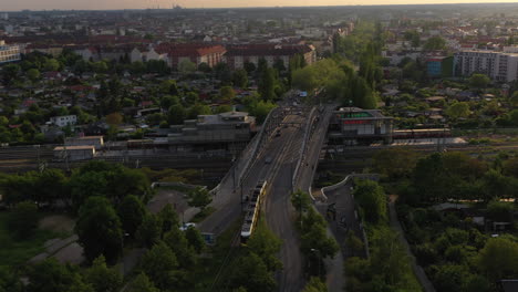 Tracking-of-tram-driving-on-Bosebrucke-bridge.-Aerial-view-of-public-transportation.-City-scene-lit-by-late-evening-sun.-Berlin,-Germany