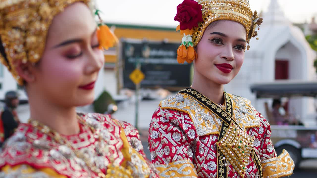 To thailandske kvinder i traditionelle dansekostumer poserer udendørs