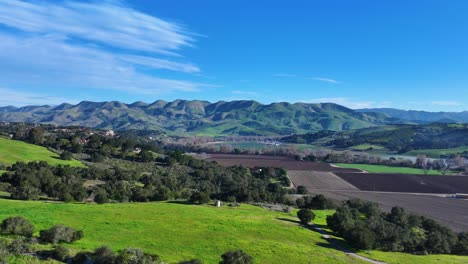 vibrant green rolling hills under blue skies in san luis obispo, california, early daylight, aerial pullback establishing