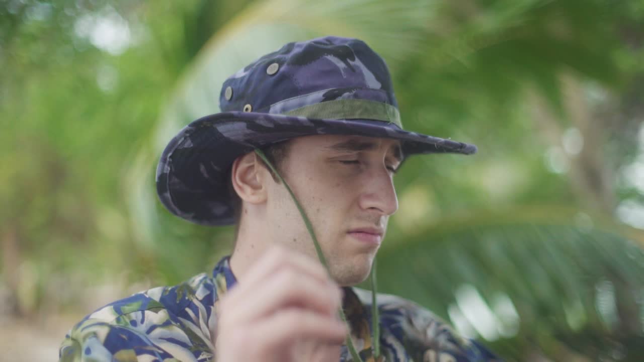 attractive white Male in Explorer costume puts on his Camouflage hat while scanning and exploring Tropical Jungle