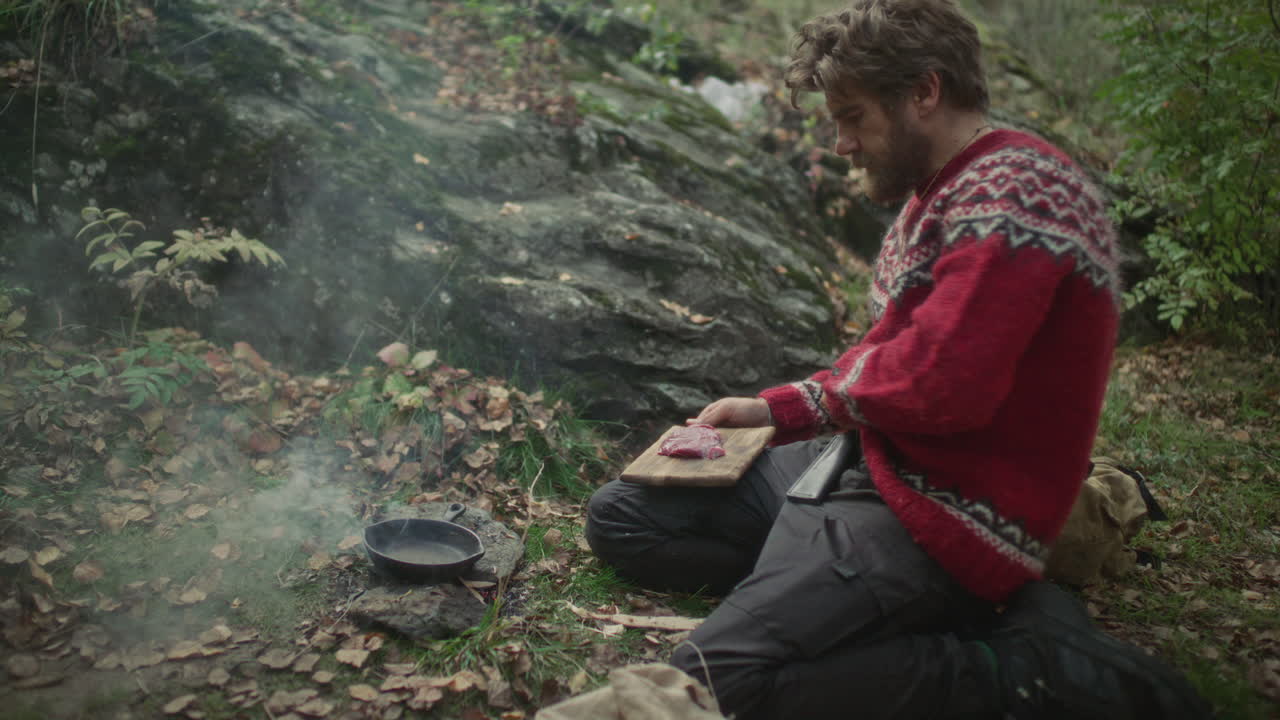 Man bereidt vlees te koken boven een kampvuur tijdens een survivaltrip in het bos