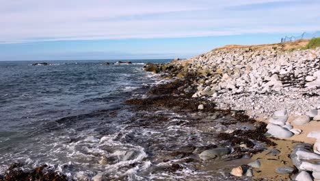 waves gently lapping a pebble and sandy beach with rocks out to sea on a bright calm day