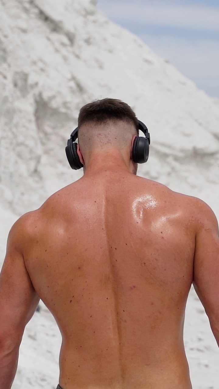 Sportsman listening music for workout. Rear view of sportman listening music with wireless headphones at training Vertical video