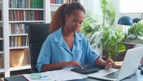 jonge afro-amerikaanse vrouw accountant gebruikt rekenmachine zit aan kantoor bureau