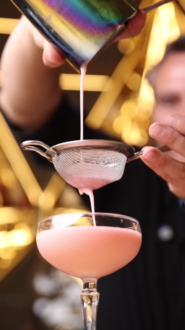 Barman che filtra e versa un cocktail rosa in un bicchiere