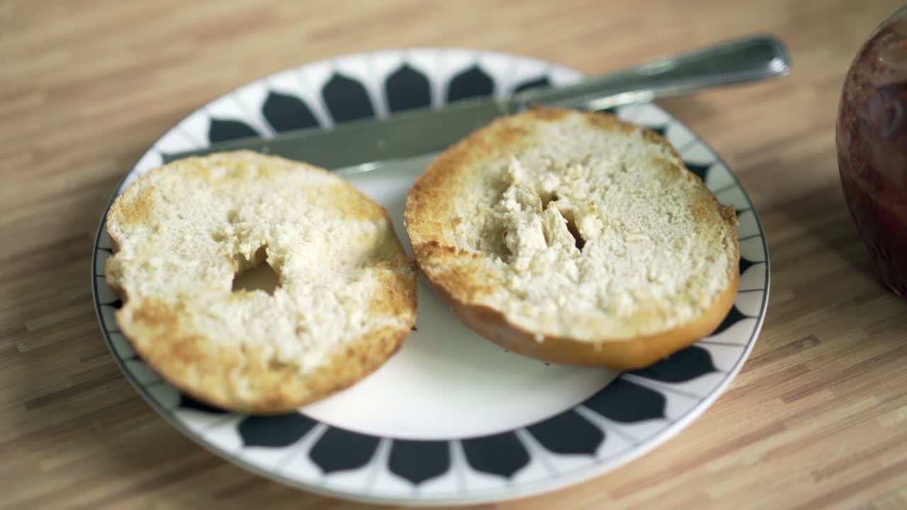 딸기 레드 젤리의 잼 냄비에서 스테인리스 스틸 나이프 움직임이 있는 흑백 접시에 구운 베이글