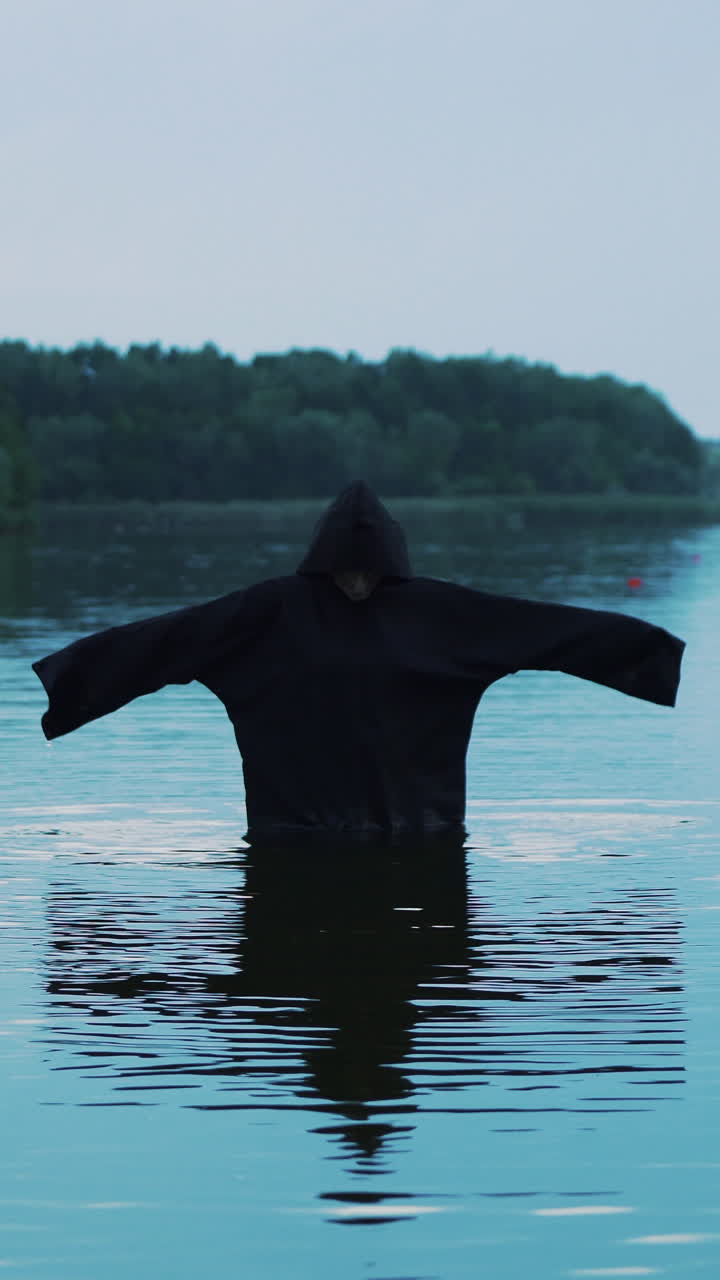 Ghost woman in the water outdoor. Scary figure in black mantle.. Vertical video