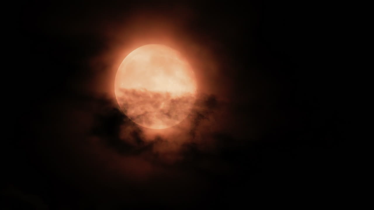 Close up of a full moon glowing through dark clouds at night