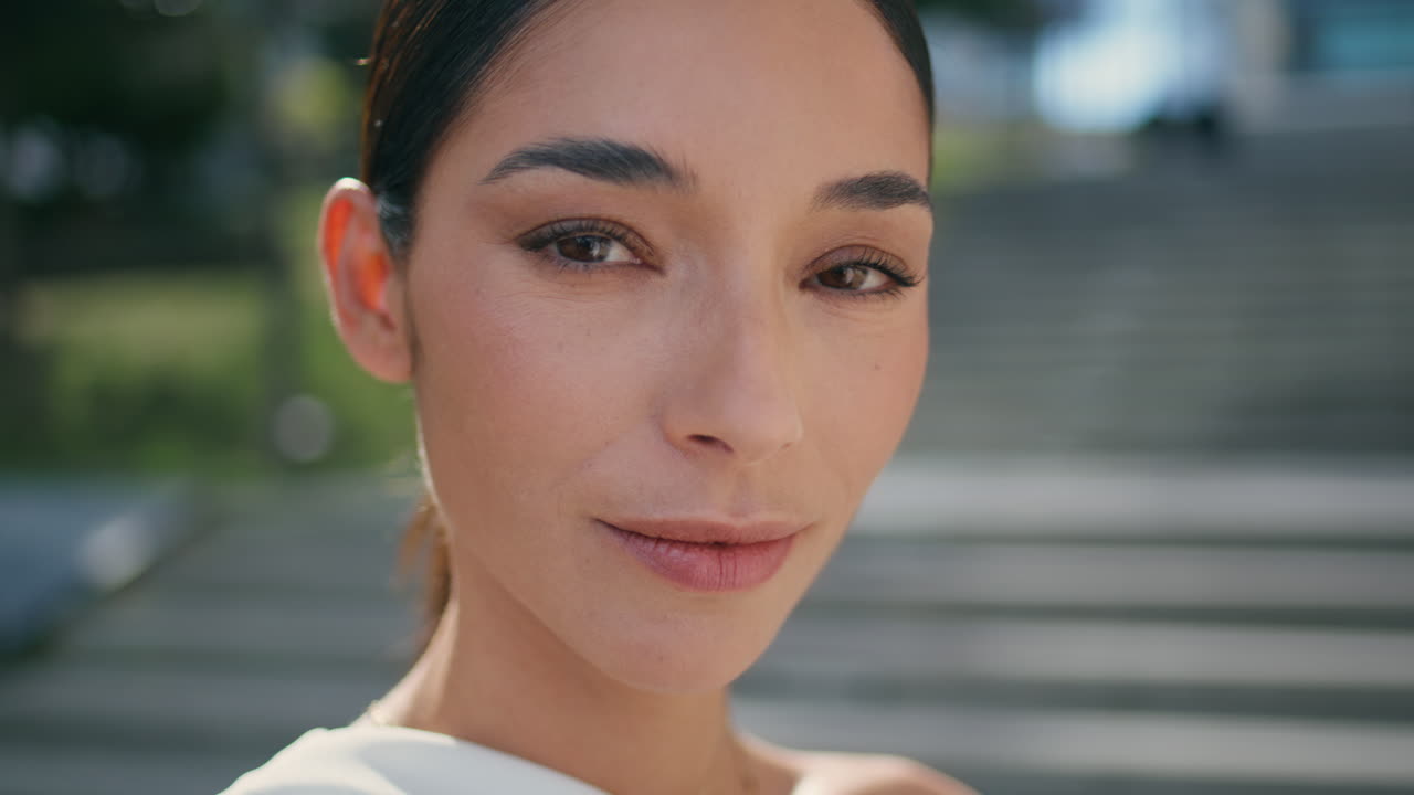 retrato de una delicada chica morena con rasgos refinados de pie en una calle soleada.